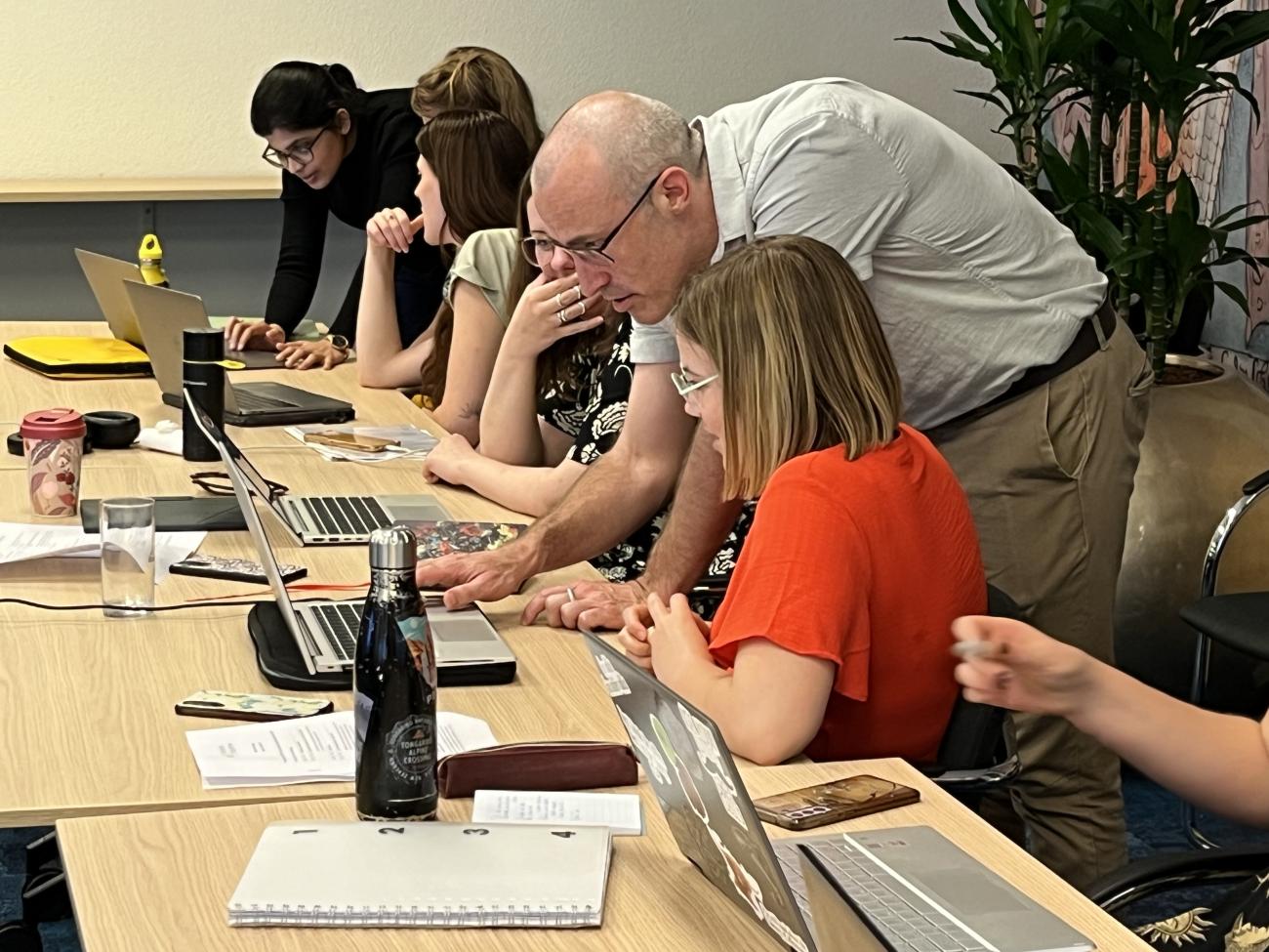 Two teachers aiding a group of students sitting behing their laptops.