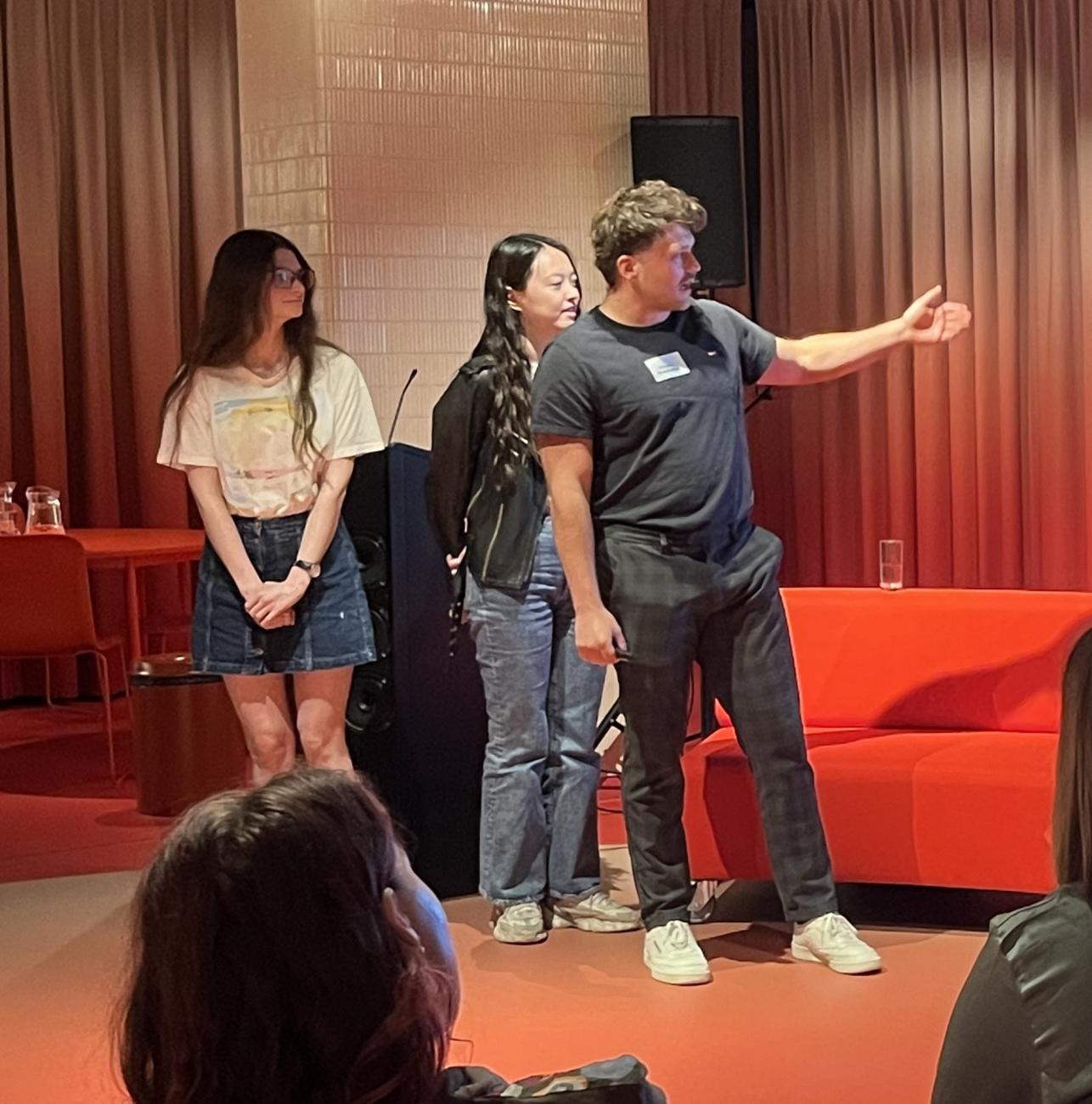 Two young woman and one young man. The man is pointing (towards the presenting screen you cannot see)