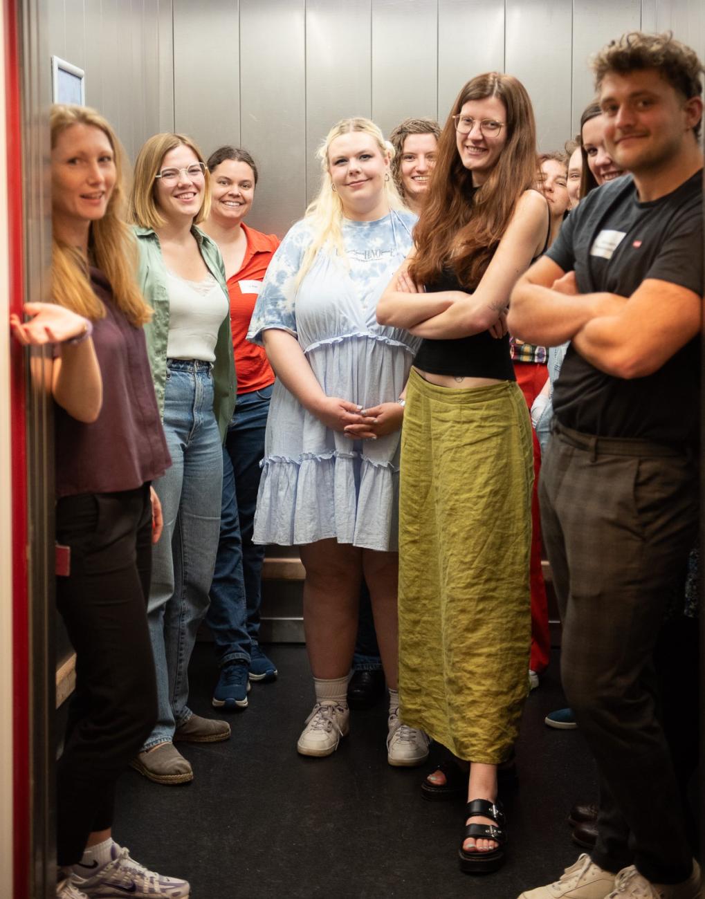 Group of people standing in an elevator, smiling for the camera