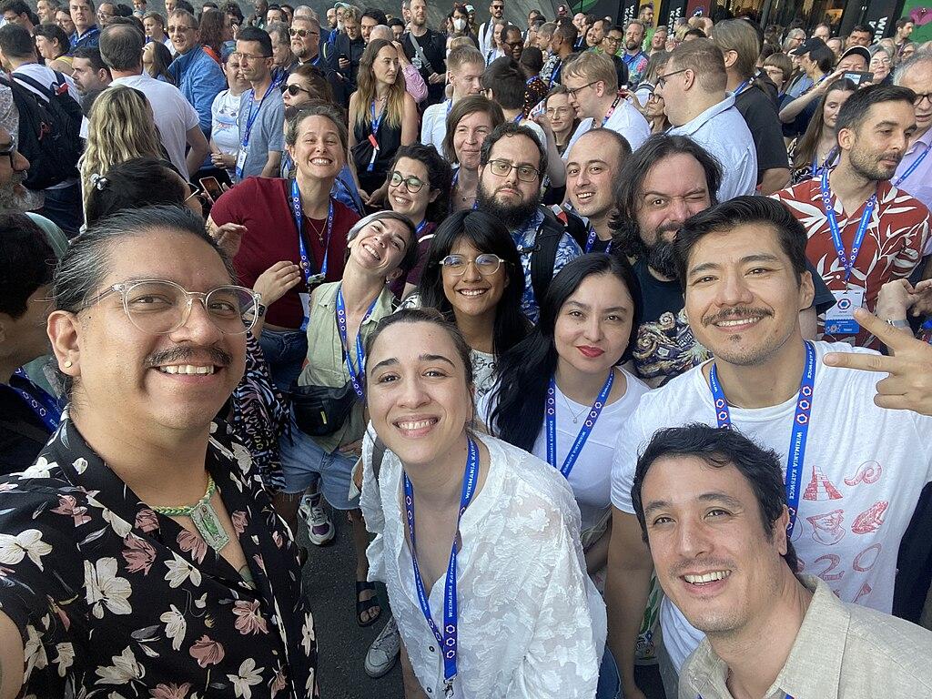 Screenshot of a lot of smiling people at a congres. All have keycards around their necks.
